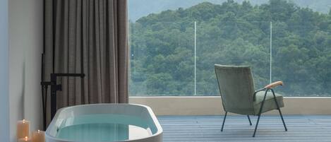A room with a bathtub, a chair, and a view of a forested hill.