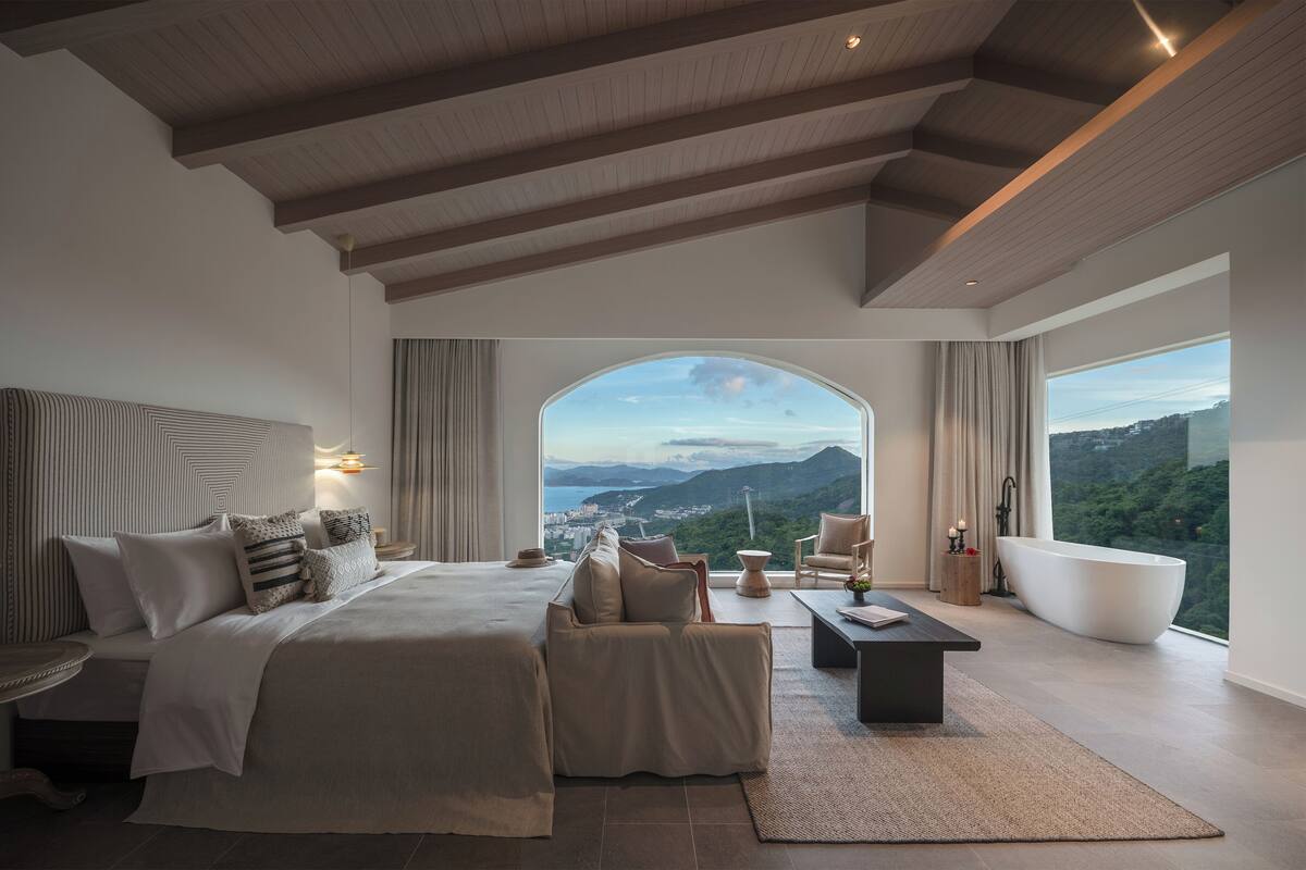 A modern bedroom with a large bed, a seating area, and a view of the mountains.