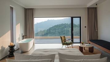 A modern bedroom with a large bed, a bathtub, a chair, and a view of a mountainous landscape.