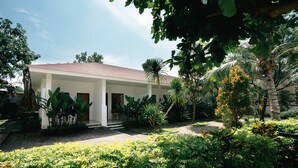 Un espace extérieur abrité, avec un bâtiment blanc, entouré d’une végétation luxuriante et de palmiers.