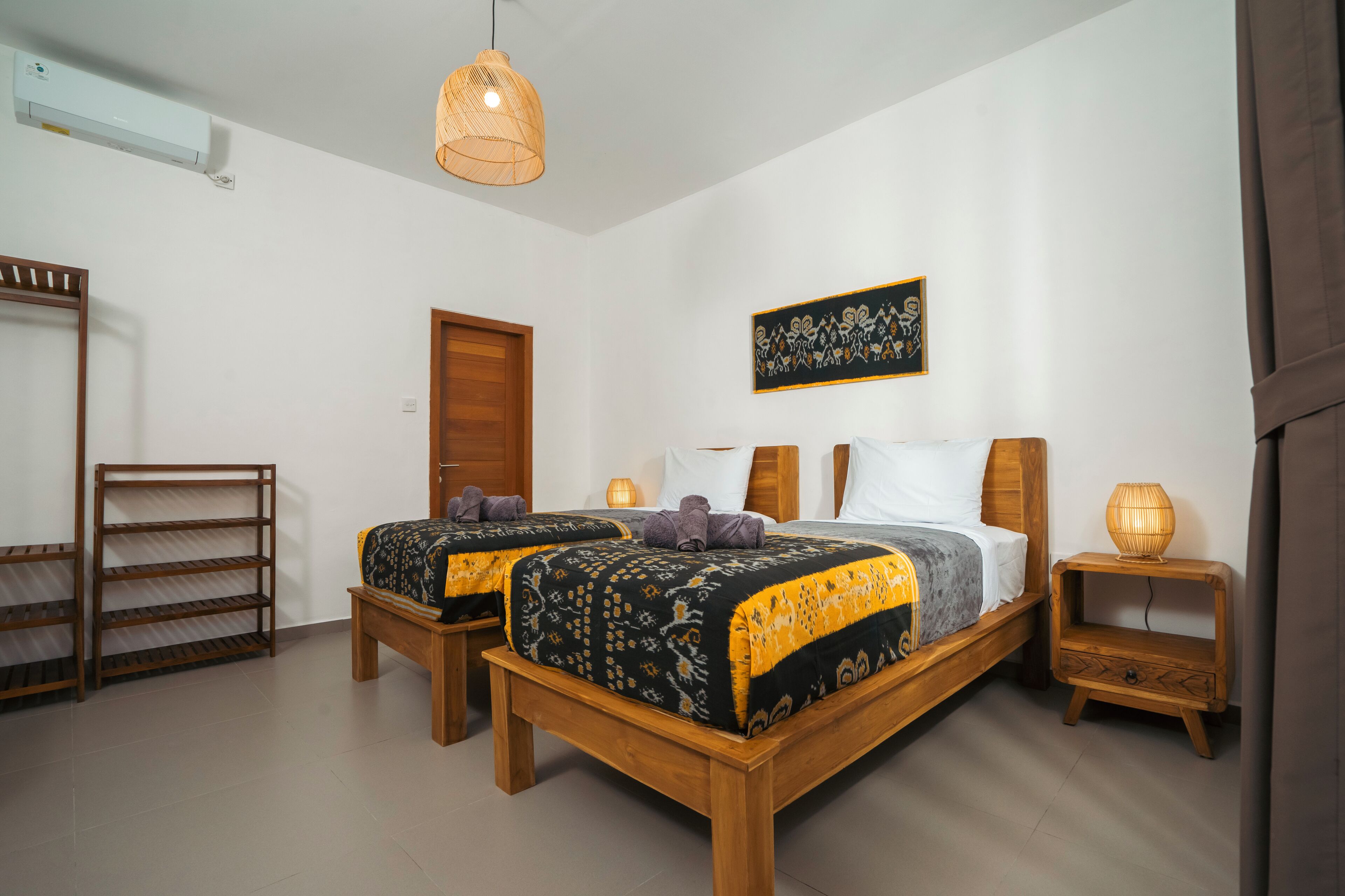 A bedroom with two beds, a wooden bench, a shelf, and a wall-mounted air conditioner.