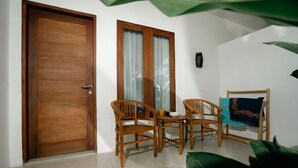 Une pièce avec une porte en bois, deux fenêtres avec des rideaux, une table en bois avec des chaises et un tableau encadré au mur.