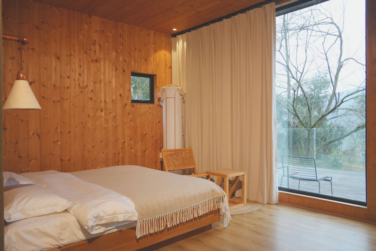 Une chambre aux murs lambrissés, comprenant un lit, une chaise, une table et une fenêtre avec des rideaux.