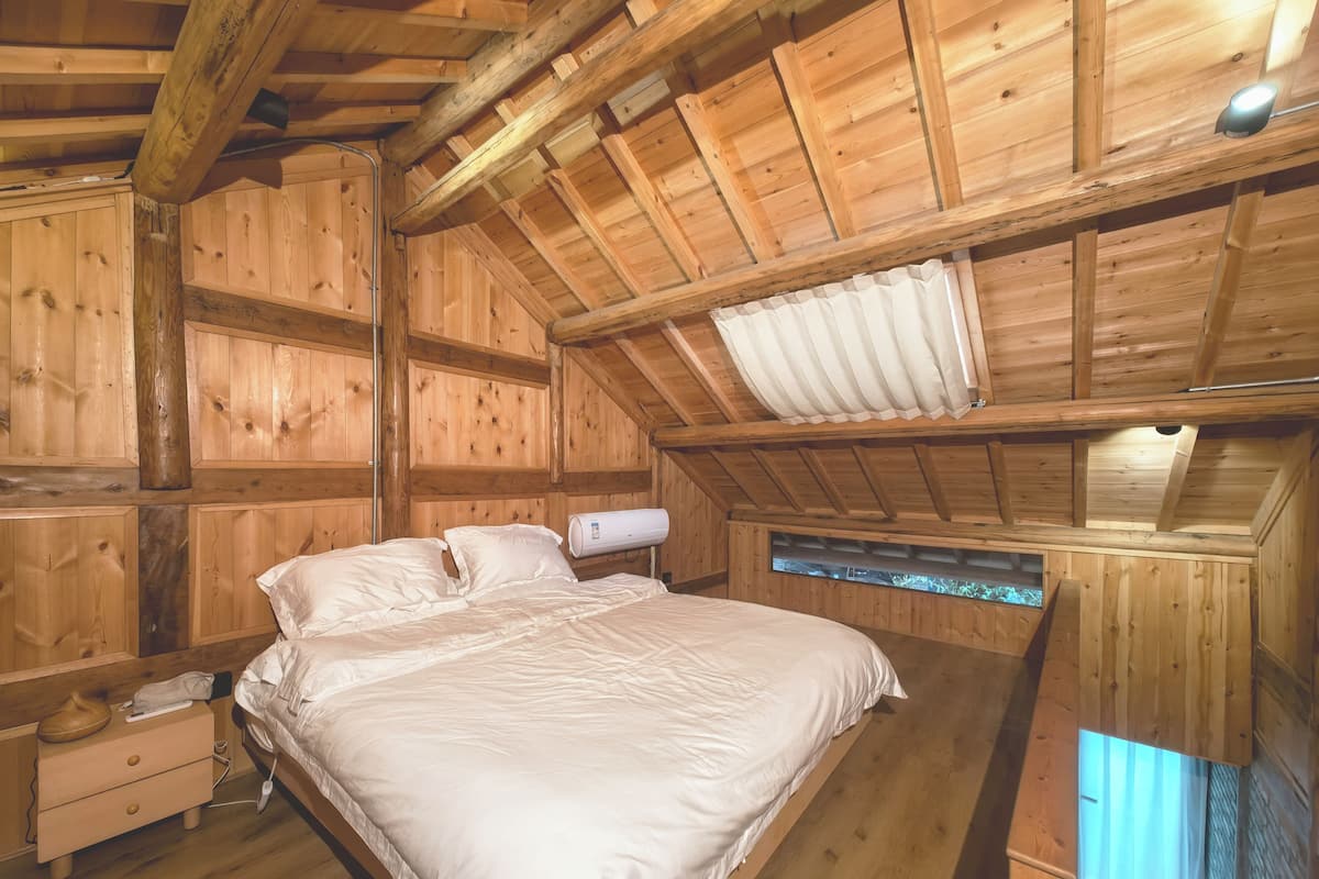 Une chambre dans une cabane en bois, avec un lit, une table de chevet, une fenêtre et un ventilateur de plafond.