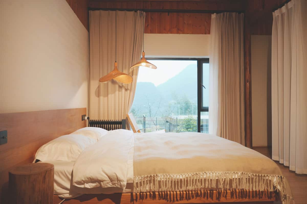 Une chambre avec un grand lit, une tête de lit en bois et une vue sur les montagnes par la fenêtre.
