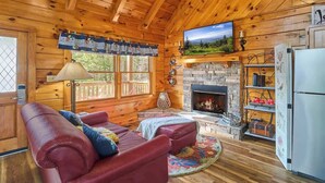 Een gezellig chalet interieur met een stenen openhaard, houten wanden, een rode leren bank en een televisie boven de openhaard.