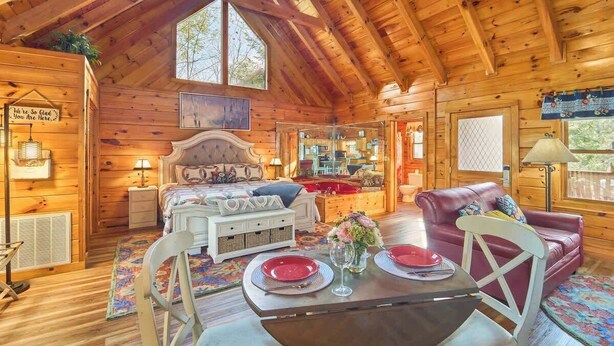 Een gezellig interieur van een chalet met een houten plafond, een bed met hoofdeinde, een eettafel met borden en een glas, en een rode leren bank.
