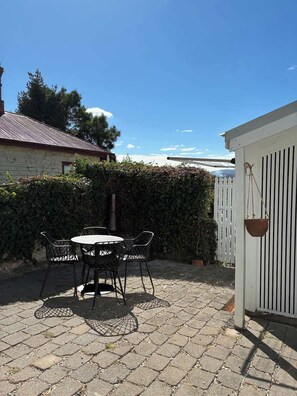 Eine Terrasse mit Tisch und Stühlen, ein weißer Zaun und ein Gebäude mit rotem Dach.