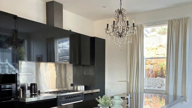 A modern kitchen with a central island, black cabinetry, stainless steel appliances, and a chandelier. - Forest Rd Haven with Tamar River Views (Trevallyn)