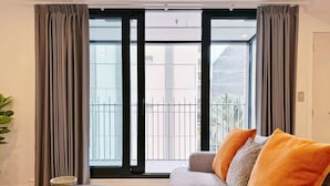 A modern living room with a grey sofa, orange cushions, a round coffee table, and a view through large windows. - Prime Location 1BR vs Aricon&Pool beside Skytower (Auckland)