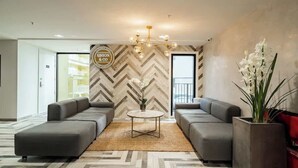 A modern hotel lobby with a herringbone-patterned wall, a central round table, two grey sofas, and a chandelier. - Incredible View Aircon 1B Studio Auckland Central (Auckland)