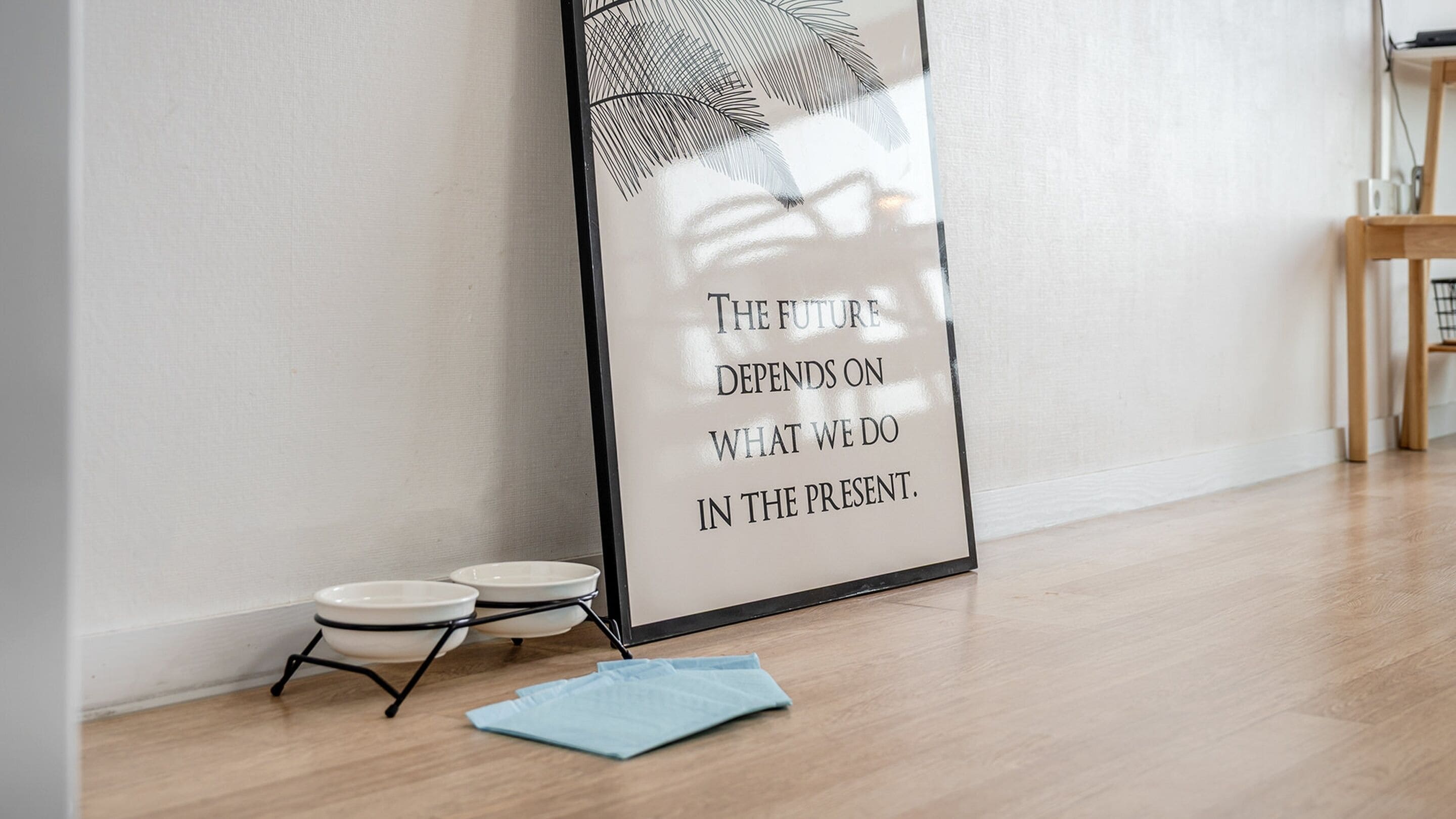 Un cadre contenant une citation inspirante accroché au mur, une petite table ronde avec un bol, et un tissu bleu posé sur le sol.