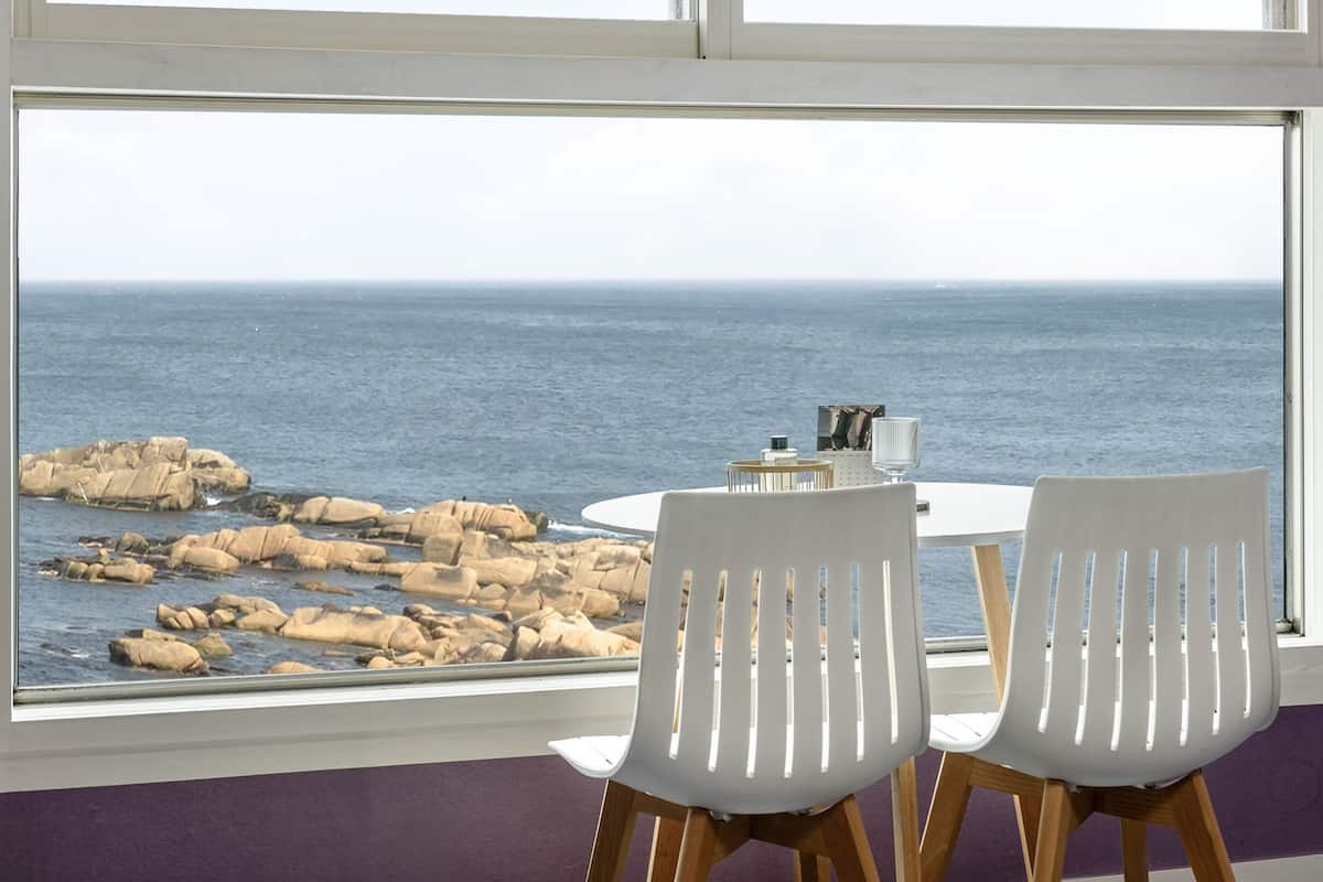 Un comedor con mesa y dos sillas, con vistas a un escarpado litoral y al mar.