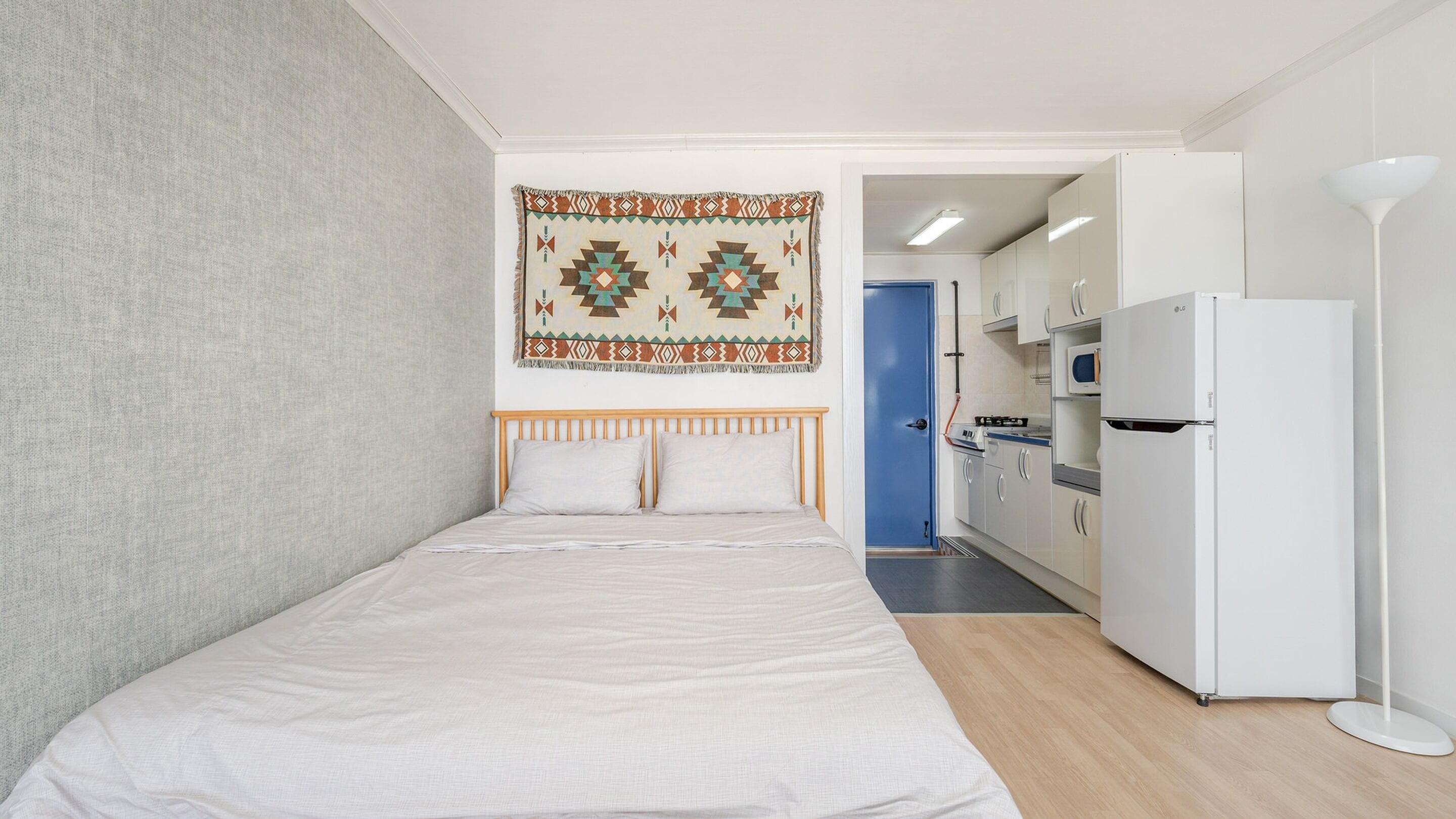 Una habitación pequeña y moderna con cama, zona de cocina y un tapiz con estampado.