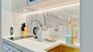 A modern kitchen with a marble backsplash, a built-in microwave, a coffee maker, and a sink with a gold faucet.
