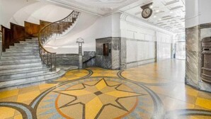 A grand lobby with a marble staircase, a star-patterned floor, and a clock on the wall.
