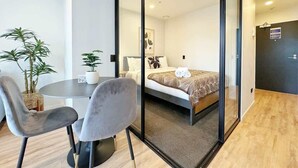 Une chambre d’hôtel moderne avec un lit, une table ronde et deux chaises, ainsi que deux plantes en pot.