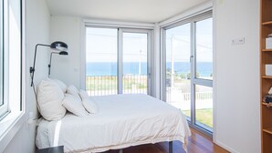 A bedroom with a large bed, a desk, and a view of the sea through a sliding glass door. - AG Villa Razo Deluxe, with swimming pool and beach 400m away (Razo Da Costa)