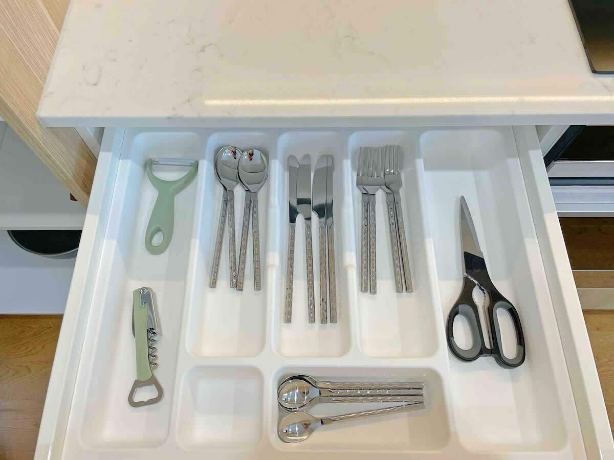 En skuffe med diverse bestik og redskaber, herunder skeer, gafler, knive og saks.
