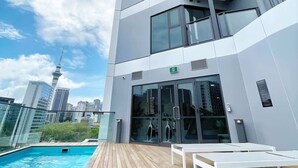 Un bâtiment moderne doté d’un espace piscine, comprenant une terrasse en bois et des chaises longues blanches.