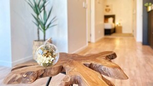Une table en bois sur laquelle est posé un vase en verre contenant des fleurs séchées, le tout placé sur un plancher en bois dans un couloir, avec une plante en arrière-plan.