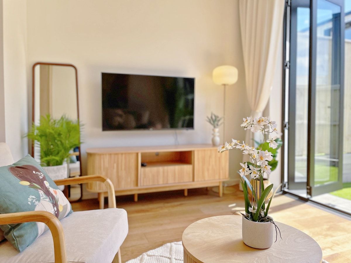 A modern living room with a flat-screen TV, wooden furniture, a round coffee table, and a potted orchid plant.