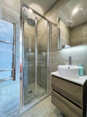 A modern bathroom with a glass shower enclosure, a white sink, and a wooden vanity.