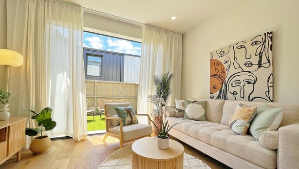 Un salon moderne avec un canapé, une table basse et un fauteuil. Il y a une grande fenêtre avec des rideaux, un tableau au mur et une plante en pot.