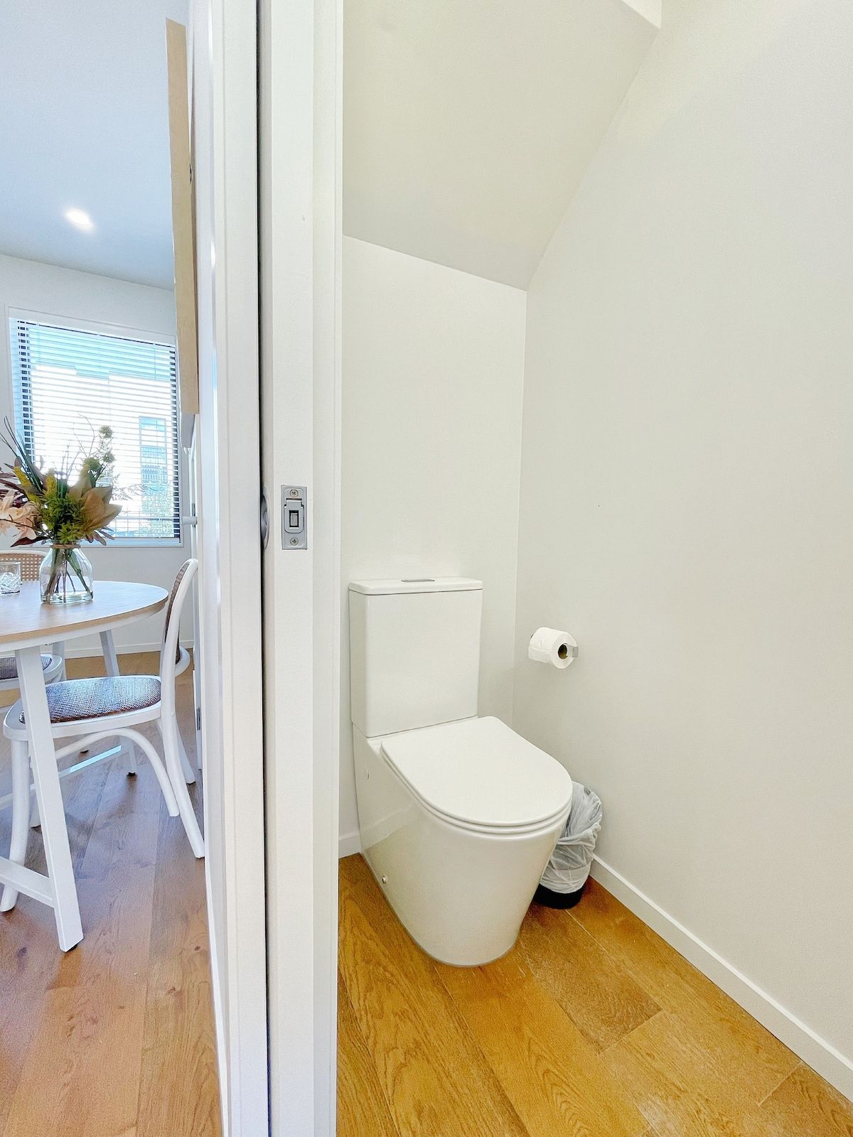 A modern bathroom with a toilet, a roll of toilet paper, and a wooden floor.