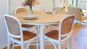 Un coin repas avec une table ronde, des chaises blanches et un vase rempli de fleurs.