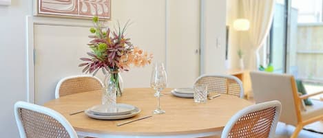 Un comedor con una mesa redonda, sillas blancas y un florero con flores.