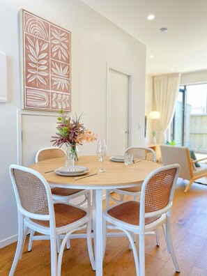 A dining area with a round table, white chairs, and a vase with flowers.