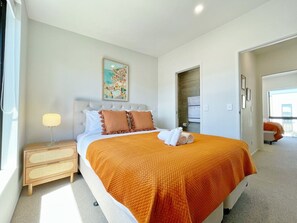 A hotel room with a bed, a nightstand, a painting, and a view through an open door.