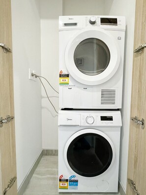 Eine übereinander gestellte Waschmaschine und Trockner mit Energie- und Wasserverbrauchskennzeichnung, angeschlossen an eine Steckdose.