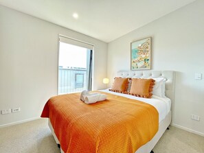 A hotel room with a large bed, a window with a view, a painting on the wall, and a lamp.