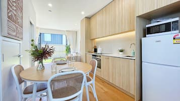 A modern kitchen with white appliances, a dining area with wicker chairs, and a view of the outdoors.