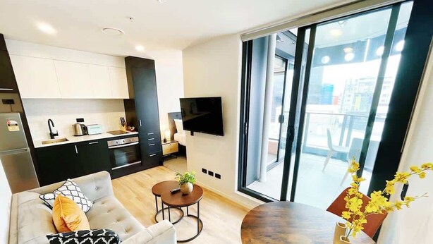 Een moderne woonkamer met een bank, salontafel en eettafel. Er is een keuken met kasten en een tv aan de muur bevestigd.