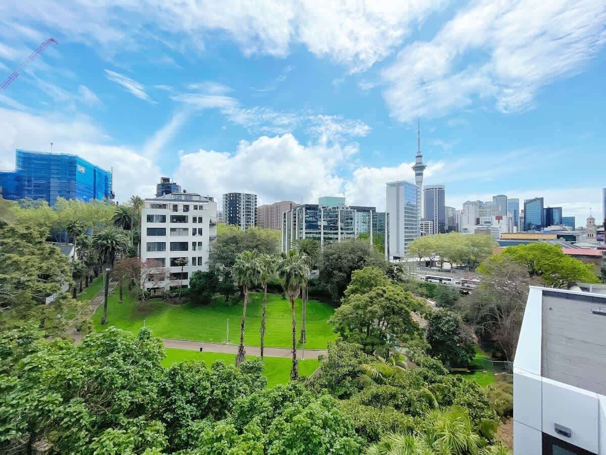 Eine Skyline mit modernen Gebäuden, einem markanten Turm und einem Parkbereich mit Bäumen.