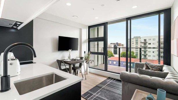 Una cocina moderna con un ventanal grande, una zona de comedor y un espacio de sala con sofá y televisor.