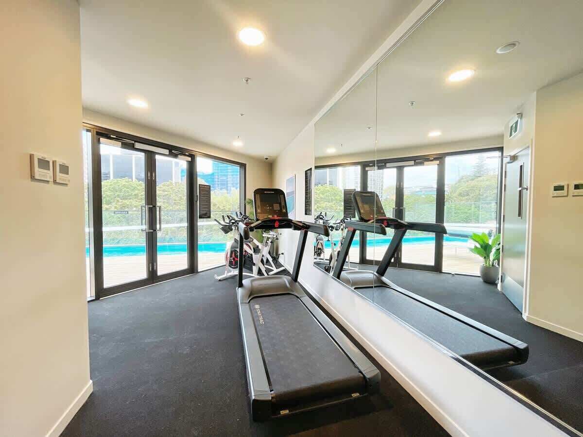 Une salle de sport moderne équipée de tapis de course et de vélos d’exercice, avec de grandes fenêtres donnant sur une piscine.
