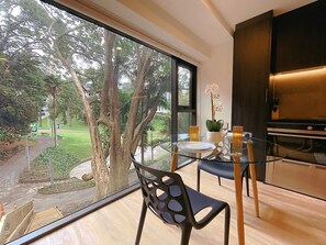 Una cocina moderna con un ventanal grande, un comedor con mesa de vidrio y vistas a un jardín.