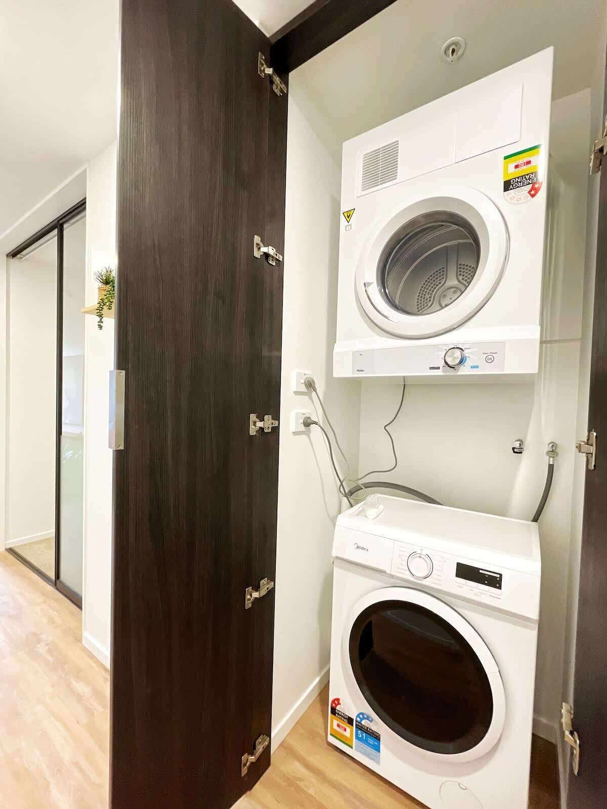 A laundry room with two stacked washing machines, a wooden door, and a visible electrical outlet.