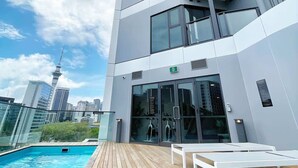 Un edificio moderno con zona de piscina, que cuenta con una terraza de madera y sillones blancos.