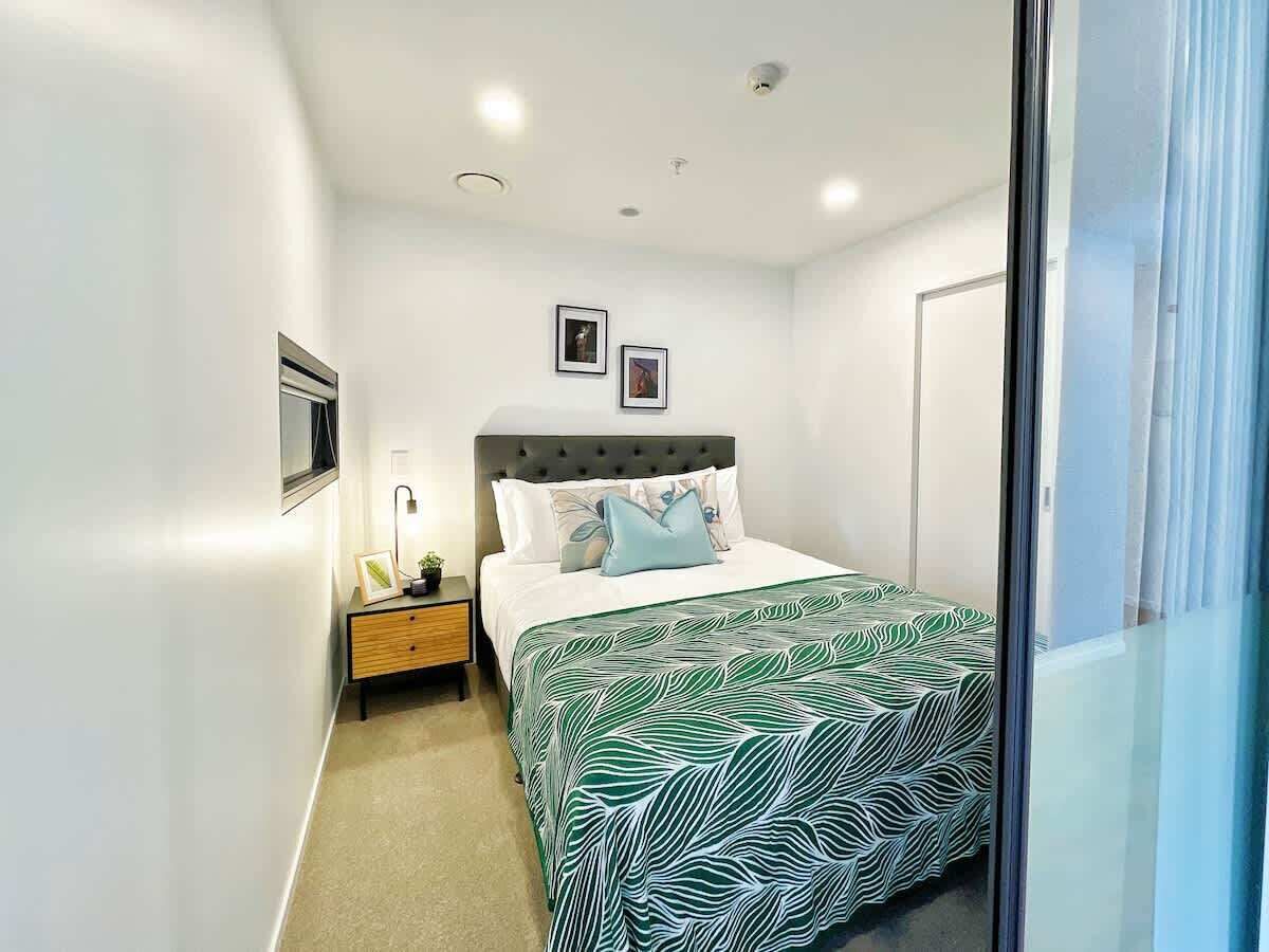 Een slaapkamer met een bed, nachtkastje en aan de muur bevestigde fotolijstjes.