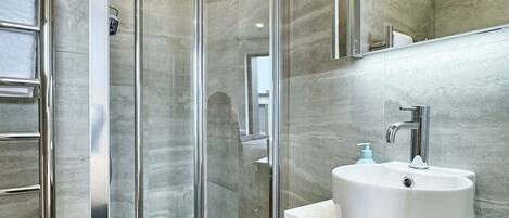 Un baño moderno con ducha envuelta en vidrio, un lavamanos blanco y un mueble de tocador de madera.