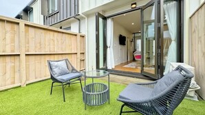 A patio with two wicker chairs and a glass table, a wooden fence, and a sliding glass door leading to an interior space. - City & Ponsonby Center Side 2 BDR Townhouse vs AC (Auckland)