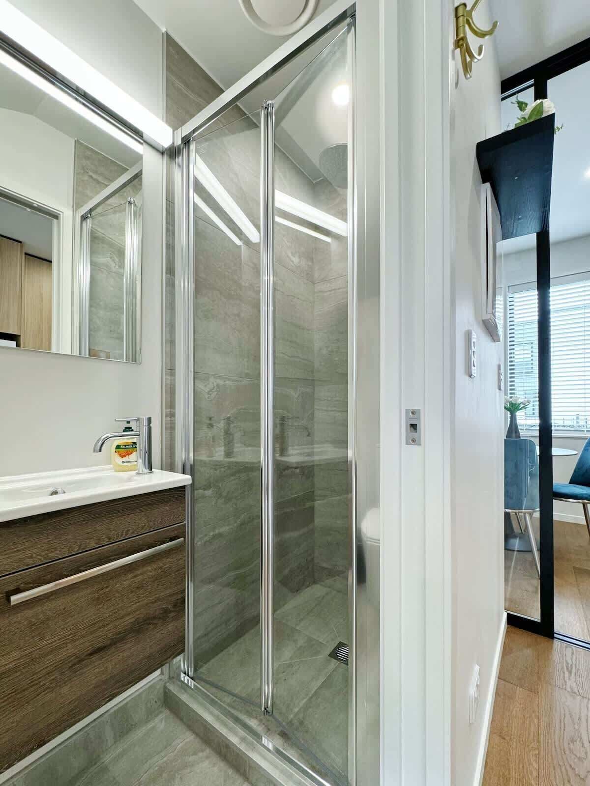 Een moderne badkamer met een douchecabine van glas, een wastafel met een marmeren blad en een grote spiegel.