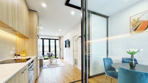 A modern kitchen with wooden cabinets, a dining area with blue chairs, and a glass partition. - City & Ponsonby Center Side 2 BDR Townhouse vs AC (Auckland)