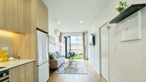 A modern kitchen with wooden cabinets, a white refrigerator, and a dining area with a sofa and coffee table. - City & Ponsonby Center Side 2 BDR Townhouse vs AC (Auckland)