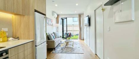 A modern kitchen with wooden cabinets, a white refrigerator, and a dining area with a sofa and coffee table.